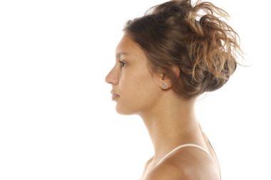 Kahverengi saçlı, beyaz bluzlu, kollu, beyaz arka planda stüdyo resmi olan genç bir kadının yan görünümü..