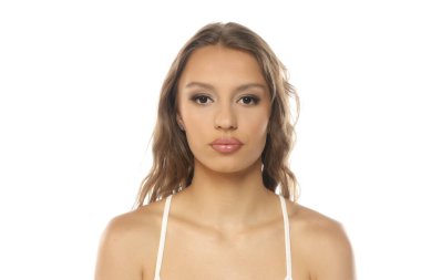 Stüdyo, beyaz arka planda dalgalı kahverengi saçlı ve nötr yüzlü genç bir kadının portresi..