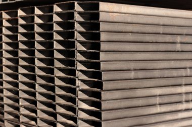 Endüstriyel metal bir depoda temiz kesilmiş kenarları olan, yığılmış kare çelikten bölüm profilleri yakın plan..