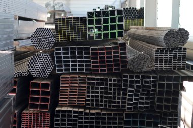 Endüstriyel metal bir deponun içinde boyutuna göre düzenlenmiş kare, dikdörtgen ve yuvarlak çelik bölme profillerinin ön görüntüsü.