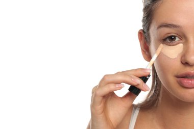 Gözünün altına aplikatör süren genç bir kadının yarım portresi. Beyaz bir arka planda stüdyo çekimi..