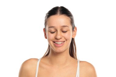 Uzun siyah saçlı, beyaz bluzlu, makyajsız, gözleri kapalı gülümseyen, beyaz arkaplanda portresi olan doğal bir kadının stüdyo fotoğrafı..