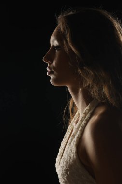 Uzun kahverengi saçlı, beyaz desenli bluzlu, siyah arka planda stüdyo resmi olan bir kadının yan görüntüsü..