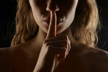 Stüdyo, uzun kahverengi saçlı bir kadının yakın plan portresini çekti. Siyah arka planda parmağını dudaklarına koydu.