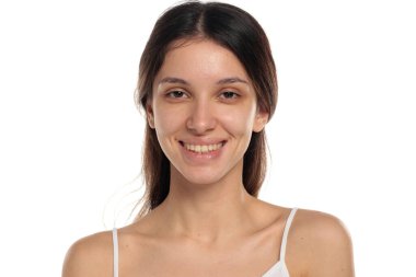 Makyajsız, doğal ten renginde gülümseyen esmer bir kadının beyaz bir arka planda kamera, portre ve vesikalık fotoğrafına baktığı bir fotoğraf..