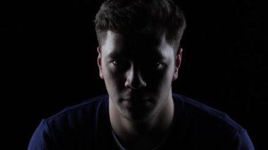 4K sinemada ciddi bir gencin karanlık portresi sessiz bir jest yapıyor ve dramatik bir şekilde gülümsemeye başlıyor.