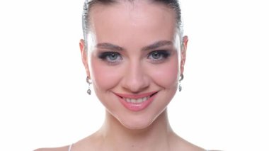 Genç kadın gülümsüyor sonra göz kırpıyor ve kameraya üflüyor, güzellik portresi, beyaz arka planda stüdyo çekimi