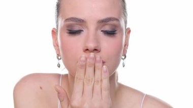 Genç bir kadın kameraya öpüşüyor, göz kırpıyor ve hava öpücüğü yolluyor, güzellik portresi, beyaz arka planda stüdyo çekimi