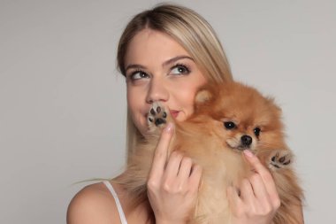 Beyaz arka planda sevimli bir köpek tutarken Pomeranya köpek patileri kokan sarışın kadının stüdyo portresi..