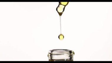 4K yavaş çekim altın kozmetik yağı pipetten cam şişeye damlıyor, makro güzellik serumu dokusu, cilt bakımı veya ilaç ürünü konsepti, beyaz arka planda stüdyo çekimi