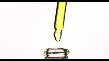 4K ağır çekimde cam şişeden pipeti çekerken, altın kozmetik yağın damlayıp geri akması, damlatıcının şişeye dönüşmesi, makro güzellik serumu, beyaz arkaplandaki stüdyo çekimi.
