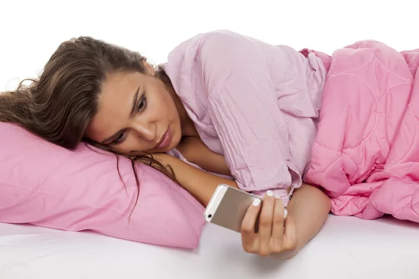Женщина лежит в постели и пишет смс по телефону — стоковое фото