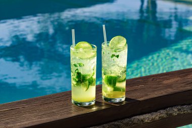 İki taze ve serin mojito, buz küpleri, limon dilimleri ve turkuaz havuzlu nane yaprakları.