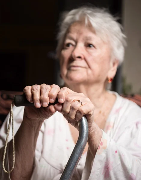 Oude vrouw zitten met een stok — Stockfoto