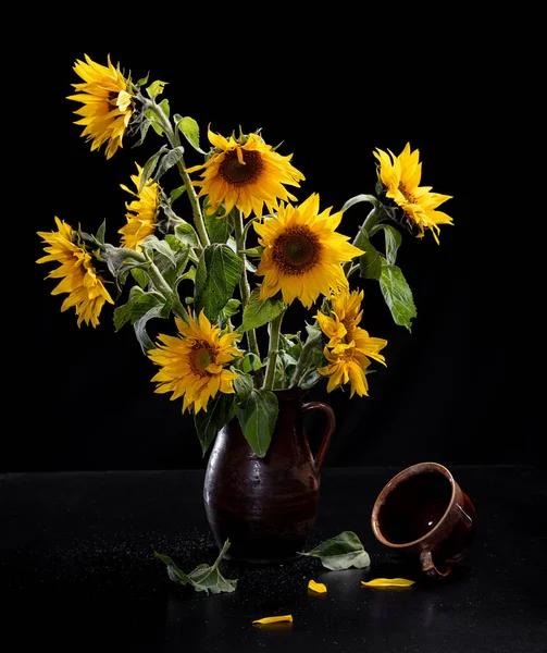 Beautiful bouquet of sunflowers in vase and tea cup on a black table over black background. Autumn still life