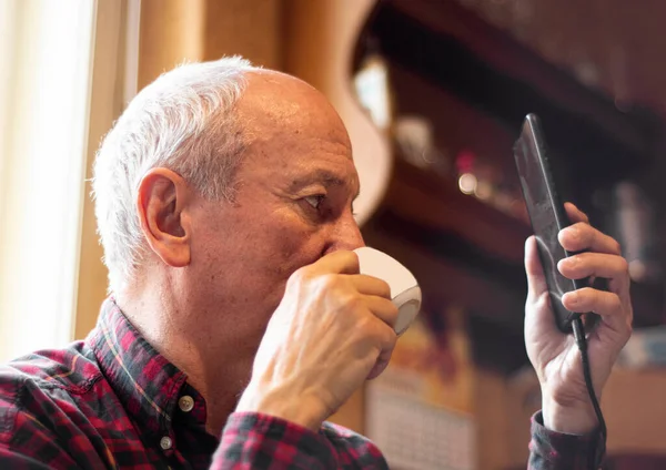 Senior Man Dricker Kaffe Och Använder Smatrphone Hemma — Stockfoto