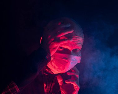 Covid-19 ve sağlık hizmeti konsepti. Tıbbi maskeli yaşlı adam dumanlı karanlık arka plan pozu verirken şok oldu.