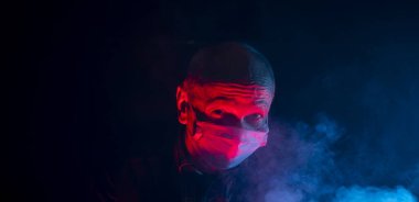 Covid-19 ve sağlık hizmeti konsepti. Tıbbi maskeli yaşlı adam dumanlı karanlık arka plan pozu verirken şok oldu.