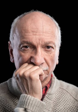 Stüdyoda karanlık arka planda poz veren düşünceli kıdemli adam.