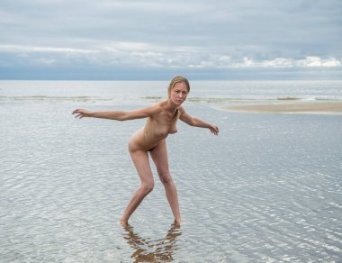 Denizde poz veren genç, güzel, çıplak bir kadın. Yazın gün batımında sahilde eğlenen seksi sarışın.