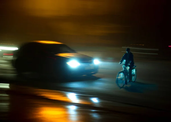 Dangerous city traffic situation with cyclist and car in the city at night in motion blur
