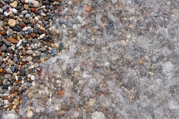 Pebble stones on the sea beach. The rolling waves of the sea with foam