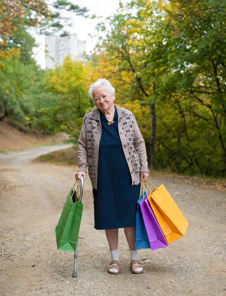 Old woman standing with shopping bags — Stock Photo, Image