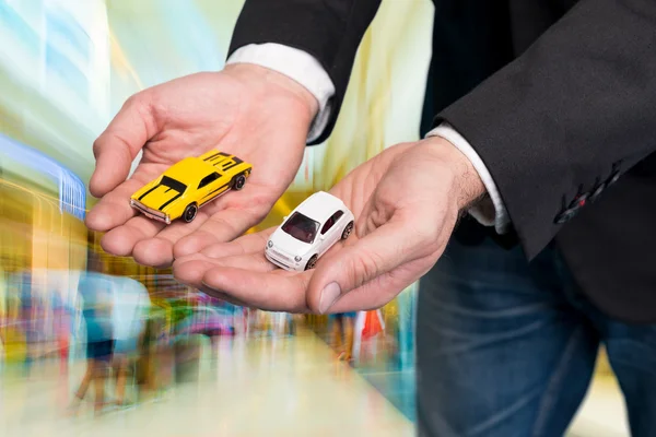Businessman in black suit holding two small car models — Stock Photo, Image