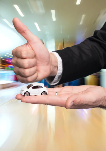 Businessman in black suit holding small car model and showing ok — Stock Photo, Image