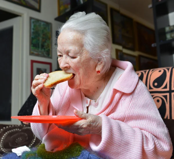 Mulher velha comendo uma fatia de pão — Fotografia de Stock