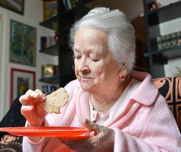 Yaşlı kadın bir dilim ekmek yemek — Stok fotoğraf