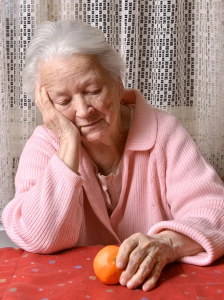 Oude vrouw kijken naar tangerine — Stockfoto
