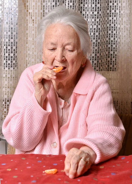 Old woman eating tangerine — Stock Photo, Image