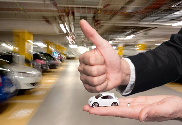 Man in black suit holding small car model and showing ok sign — Stock Photo, Image