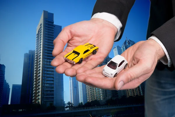 Businessman in black suit holding two small car models — Stock Photo, Image