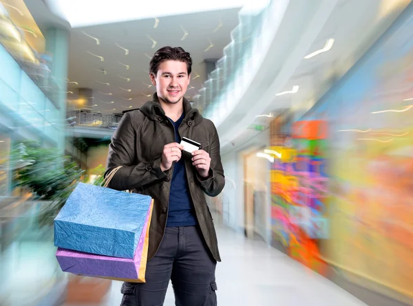 Lachende knappe man met shopping tassen en credit card — Stockfoto