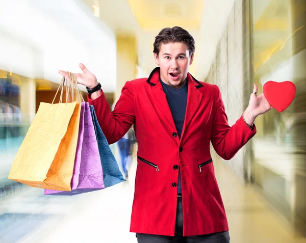 Sorrindo homem bonito segurando sacos de compras e coração vermelho — Fotografia de Stock