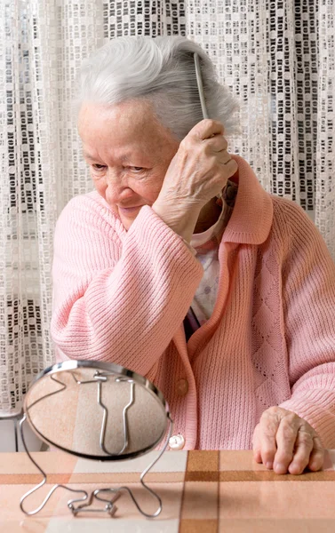 Oude lachende vrouw thuis haar haren kammen — Stockfoto