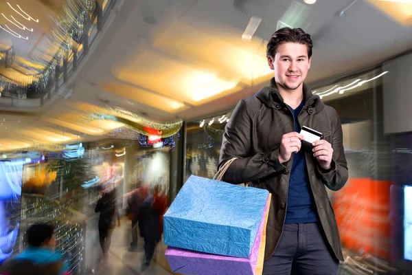 Uomo bello sorridente con borse della spesa e carta di credito — Foto Stock