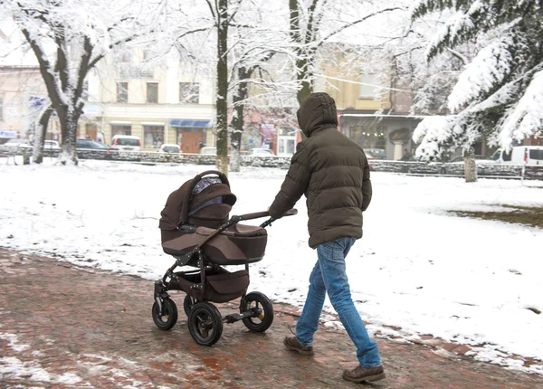 Padre con un niño pequeño en el cochecito caminando por la calle . —  Fotos de Stock