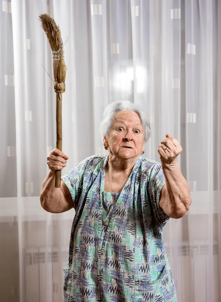 Old angry woman threatening with a broom — Stock Photo, Image