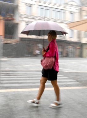 Şiddetli yağmurda caddede hızla yürüyen bir kadın, elinde hareket halinde büyük bir şemsiye, bulanık.