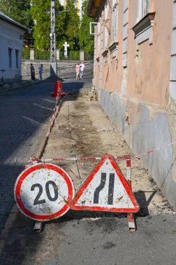 Road signs showing a speed limit of 20 and warning of a narrow road stand on a street undergoing construction