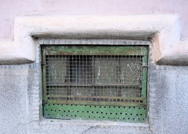Yıpranmış yeşil pencere ızgarası, tarihi bir bölgedeki eski bir binanın dokusunu ve karakterini vurgulayan çatlak bir taş duvara kurulur. 