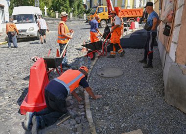 UZHOROD, UKRAINE - 13 Ağustos 2025: Güneşli öğleden sonra kentsel bölgede kaldırım taşları tamir eden inşaat işçileri