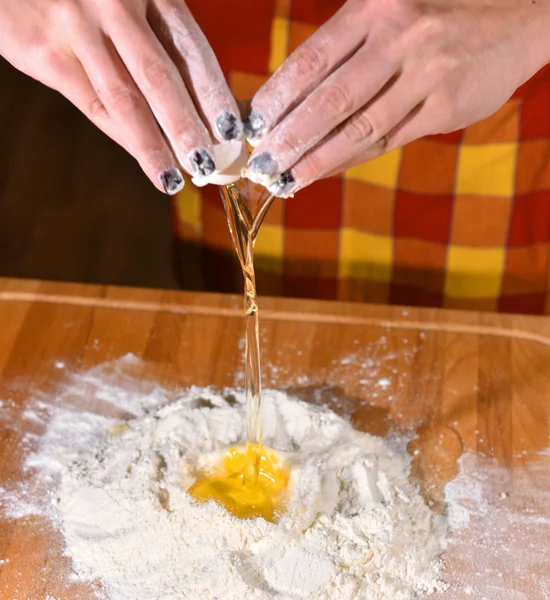 Frau fügt Ei zum Mehl hinzu — Stockfoto