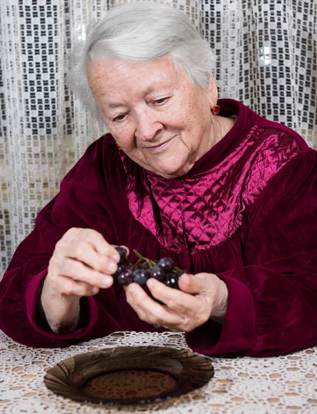 Smiling old woman eating grapes — Stock Photo, Image