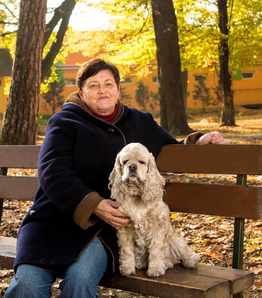 Mulher sênior sentada em um banco com um cão — Fotografia de Stock