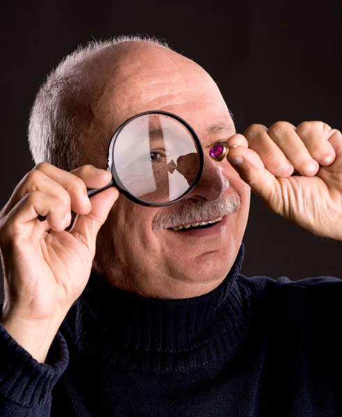 Senior jeweler looking at jewelry through magnifying glass — Stock Photo, Image