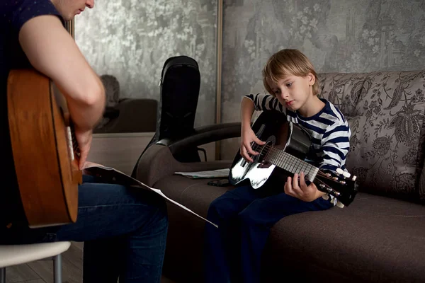 Un jeune musicien apprend à un petit garçon à jouer de la guitare acoustique et à jouer par notes — Photo